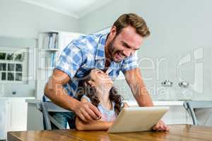 Cheerful father and daughter using digital tablet at table