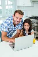 Happy man with daughter using laptop in kitchen