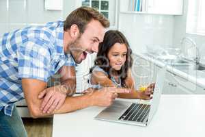 Surprised father with daughter using laptop in kitchen
