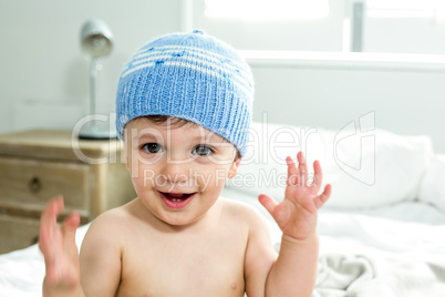 Shirtless baby boy wearing knit hat in bedroom