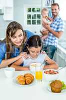 Mother looking at daughter having breakfast in kitchen