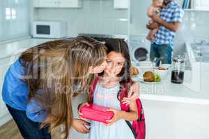 Mother kissing girl holding school lunch box