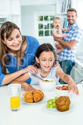 Woman looking at daughter having breakfast in kitchen