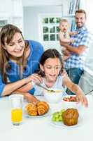 Woman looking at daughter having breakfast in kitchen