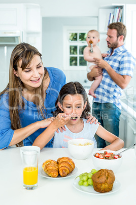 Smiling mother looking at daughter having breakfast in kitchen