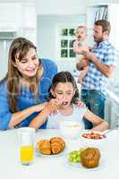 Smiling mother looking at daughter having breakfast in kitchen