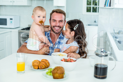 Smiling man with two children having breakfast in kitchen
