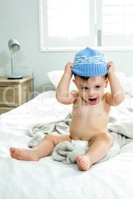 Cute baby boy wearing knit hat on bed