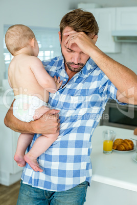 Worried man holding baby boy in kitchen at home