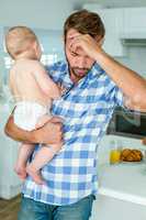 Worried man holding baby boy in kitchen at home
