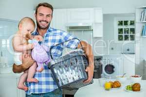 Father carrying playful son while holding basket by table
