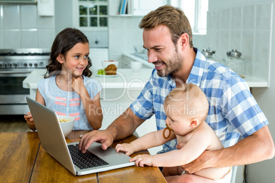Happy father using laptop while taking care of children