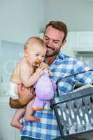 Father carrying playful son while holding basket in kitchen