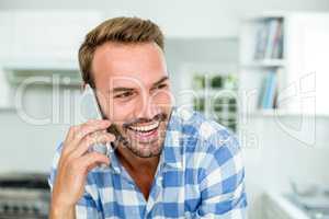 Happy handsome man talking on cellphone in kitchen