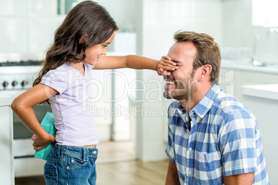 Girl hiding gift while covering happy father eyes