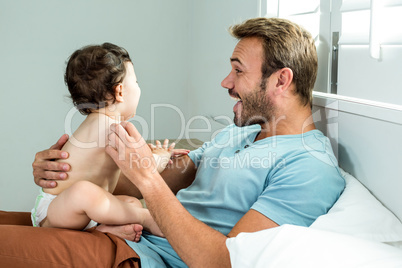 Father playing with baby boy on bed at home