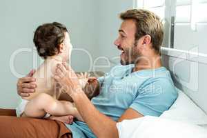 Father playing with baby boy on bed at home