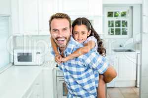 Happy father carrying daughter on back in kitchen