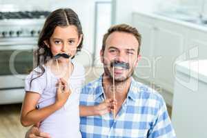 Father and daughter with artificial mustache at home