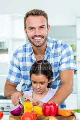 Father assisting daughter in cutting vegetables at home