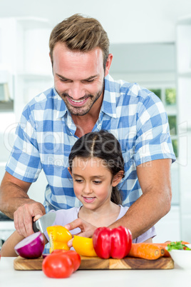 Father assisting daughter in chopping vegetables