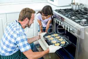 Father placing cookies in oven while daughter looking