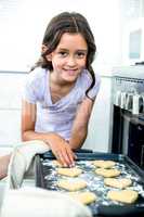 Girl smiling while touching heart shape cookies in tray