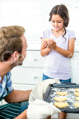 Girl holding cookie while father looking at her in kitchen