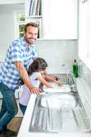 Man with daughter washing utensils at kitchen sink