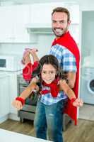 Happy father lifting girl in superhero costume at home
