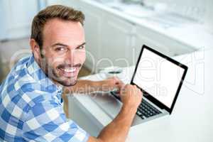 Happy man using laptop while sitting at table in kitchen