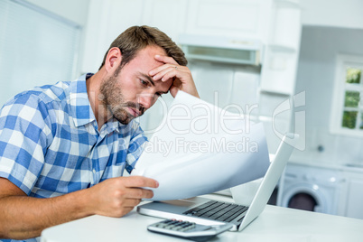 Tensed man looking in documents while sitting by laptop at table