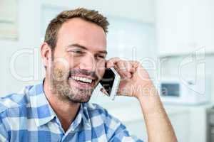 Happy man talking on cellphone while sitting in kitchen