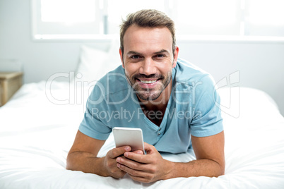 Happy man using cellphone on bed at home