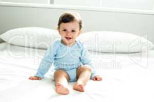 Cute baby boy sitting on bed at home