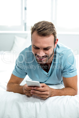 Happy man using cellphone while lying on bed