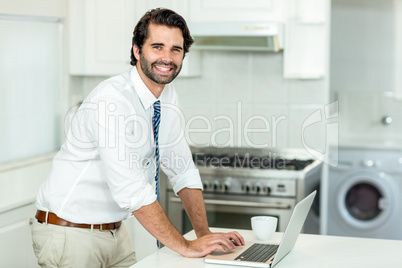 Happy businessman using laptop at table in kitchen