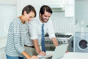 Couple looking in laptop while standing by table in kitchen