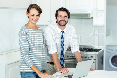 Happy couple with laptop standing by table in kitchen