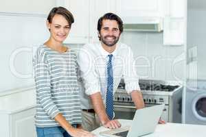 Happy couple with laptop standing by table in kitchen