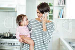 Mother talking on smartphone with daughter in kitchen