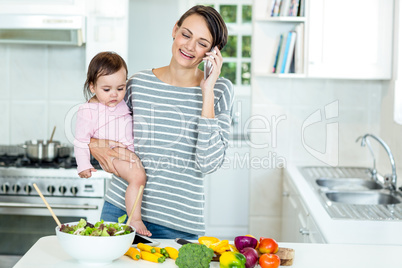 Happy woman carrying daughter while talking on cellphone