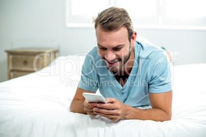 Happy man using cellphone on bed