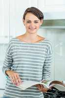 Pretty woman smiling while reading book in kitchen