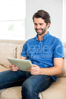 Man using digital tablet while sitting on sofa at home