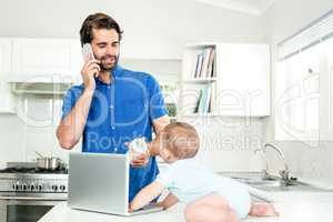 Man talking on mobile phone while feeding son at table