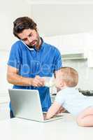 Man talking on cellphone while feeding son at table