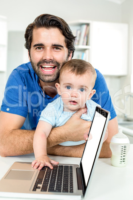 Happy father with son leaning by laptop at table