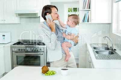 Businesswoman talking on cellphone while playing with son