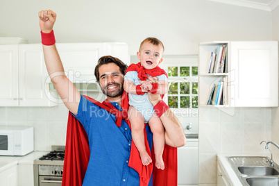 Father in superhero costume lifting son in kitchen